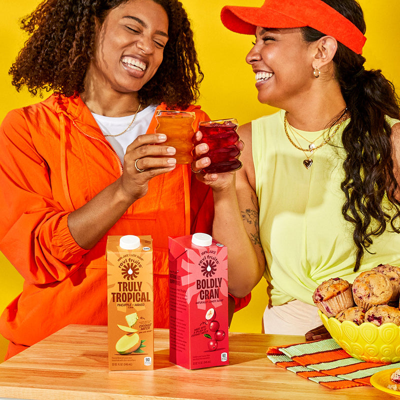 Two smiling people clinking glasses of Revl Fruits juice.